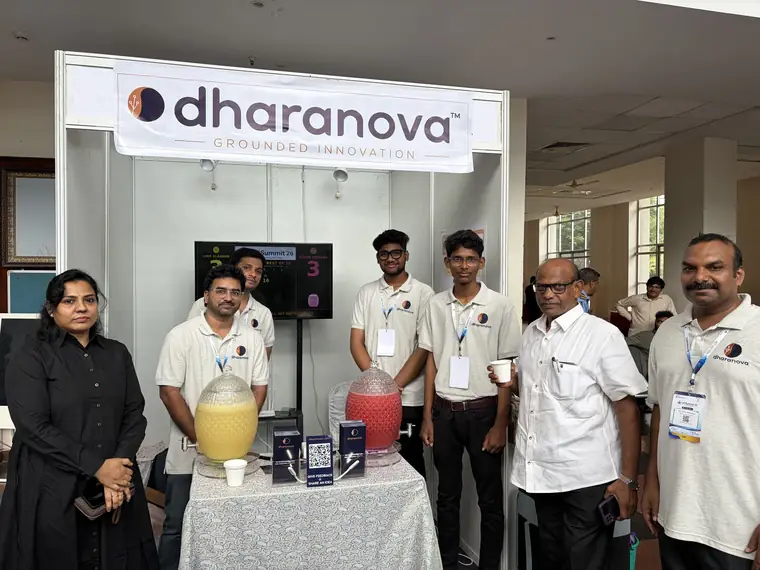 The Dharanova team standing with visitors in front of the booth and the two juice jars.