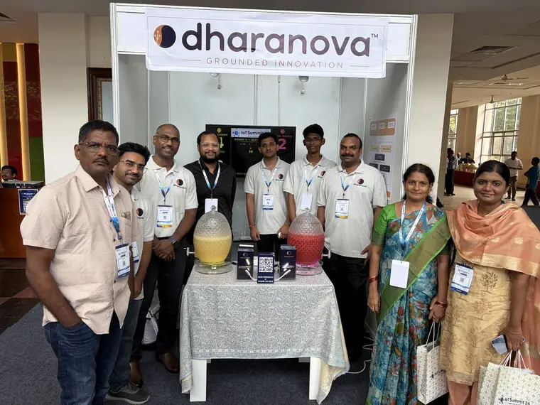 A larger group of Dharanova engineers and visitors gathered in front of the booth at the end of the day.