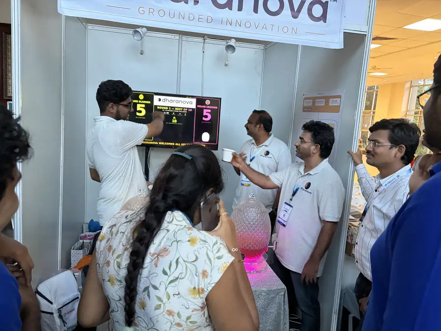 Visitors and Dharanova engineers around the booth scoreboard showing a five all tie during a round.