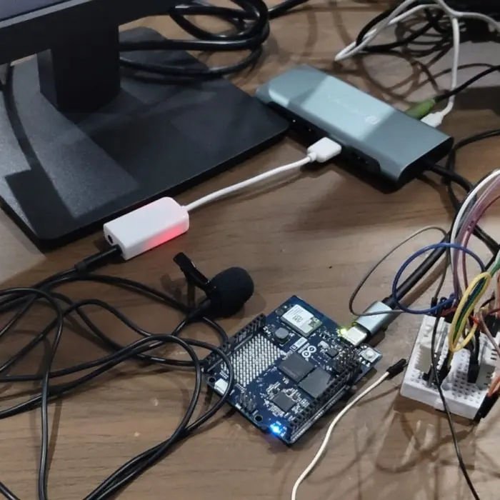 The Arduino UNO Q board on a desk with a USB lavalier microphone and sensor wiring.