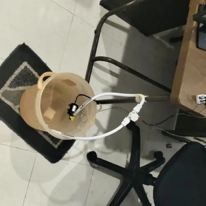 A hall-effect flow sensor fitted in-line on tubing running from a plastic tub, on an office floor.